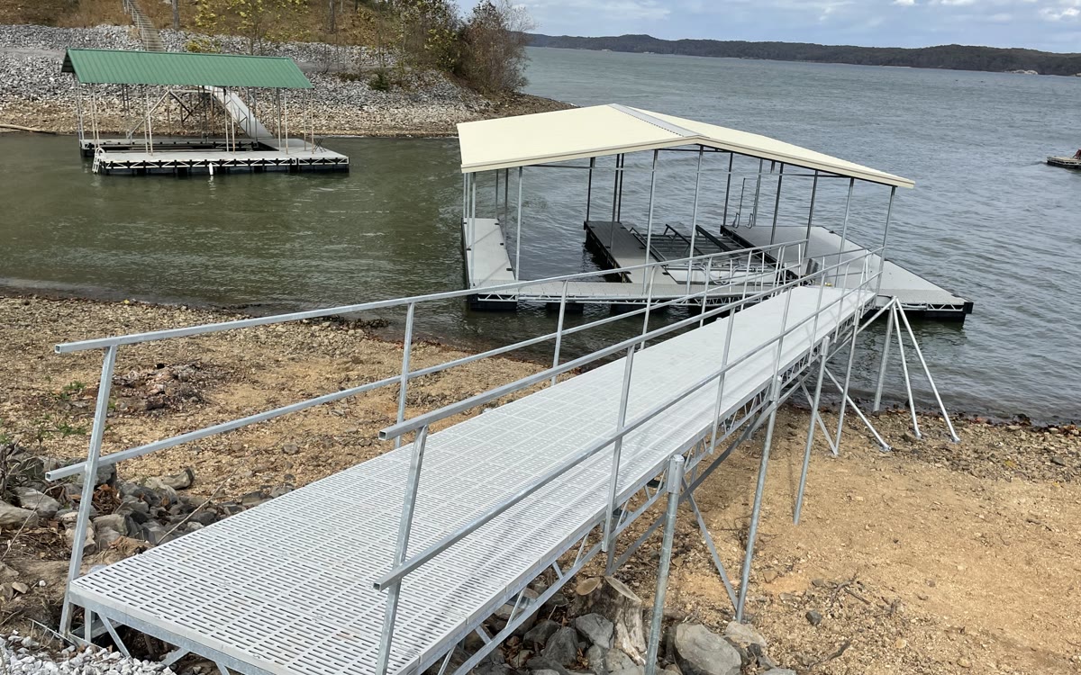 A long aluminum gangway running from a riprap bank out to a covered Twin Lakes boat slip